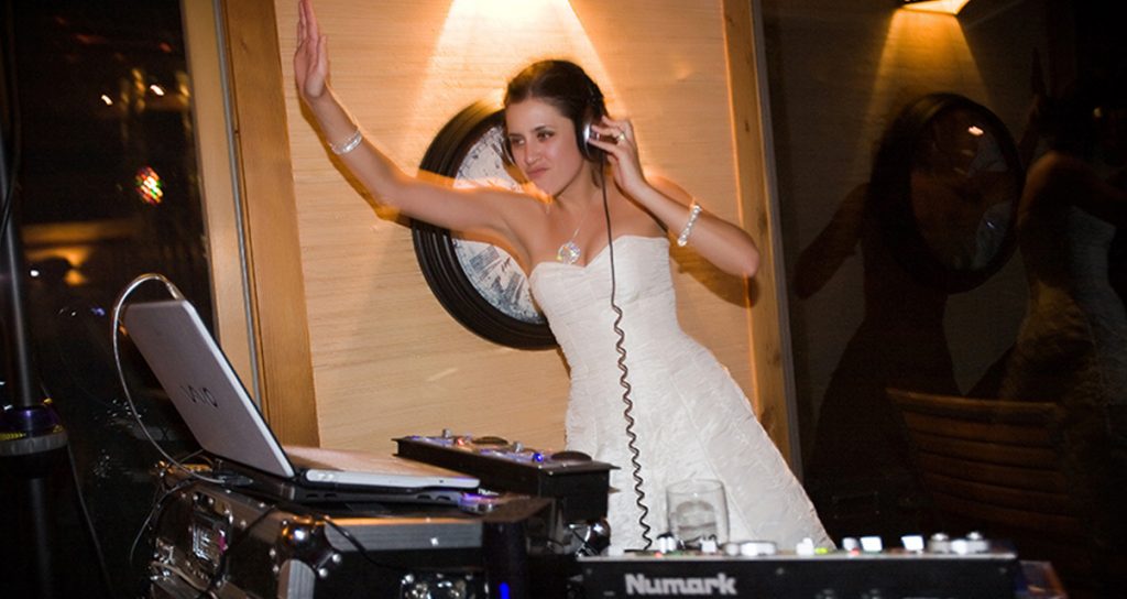 DJ performing at wedding party with guests dancing and vibrant lighting setup